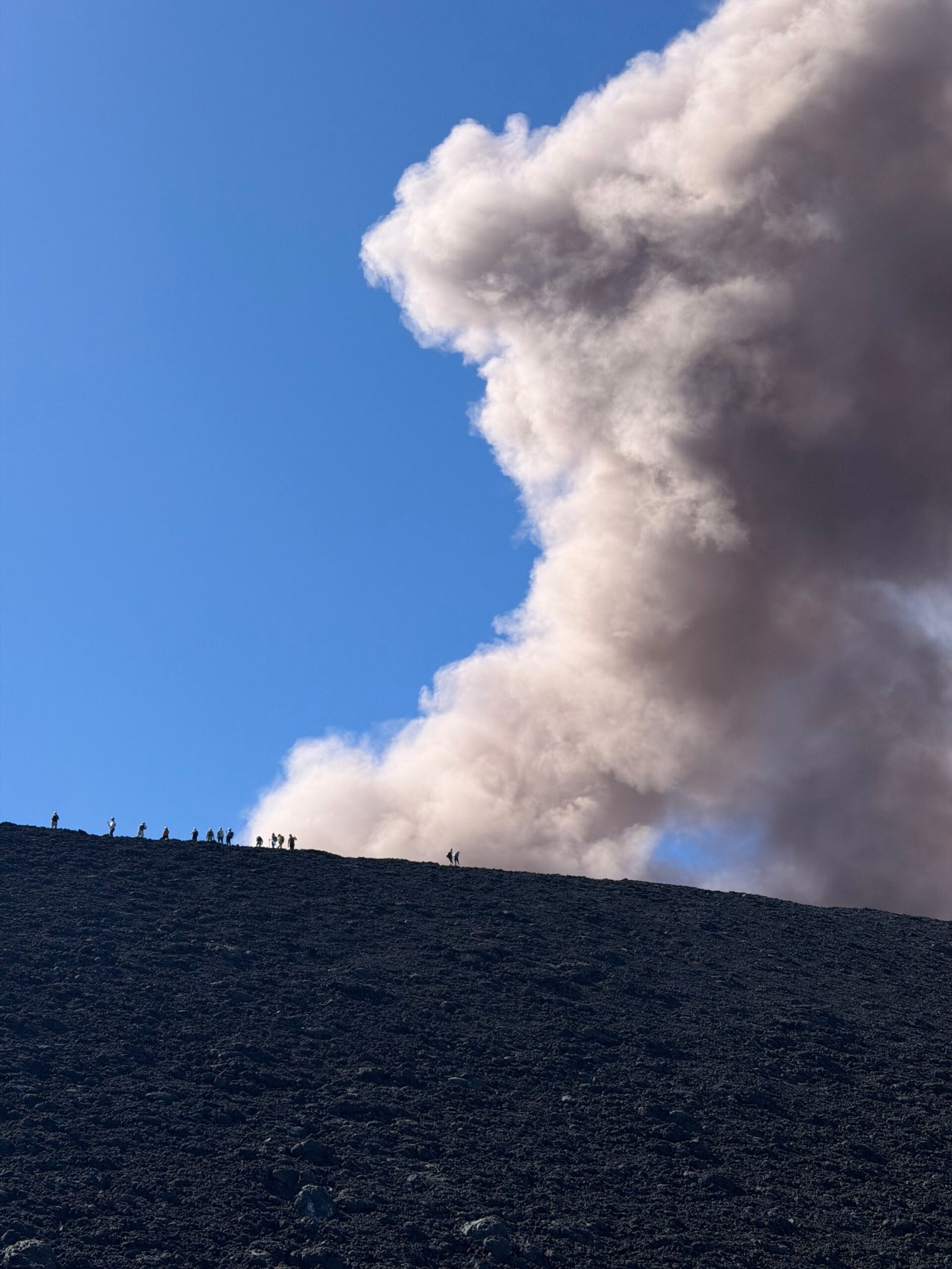 Randonneurs sur une crête dans la zone sommitale de l’Etna, sous une colonne de cendres