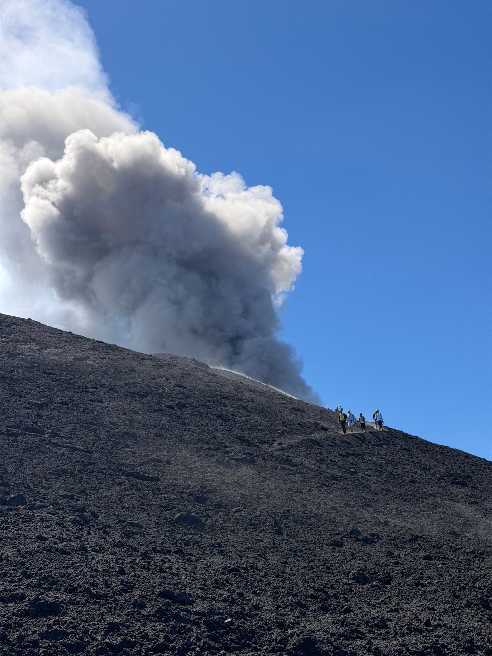 Pente volcanique en haute altitude sur l’Etna avec des randonneurs et un panache de cendres